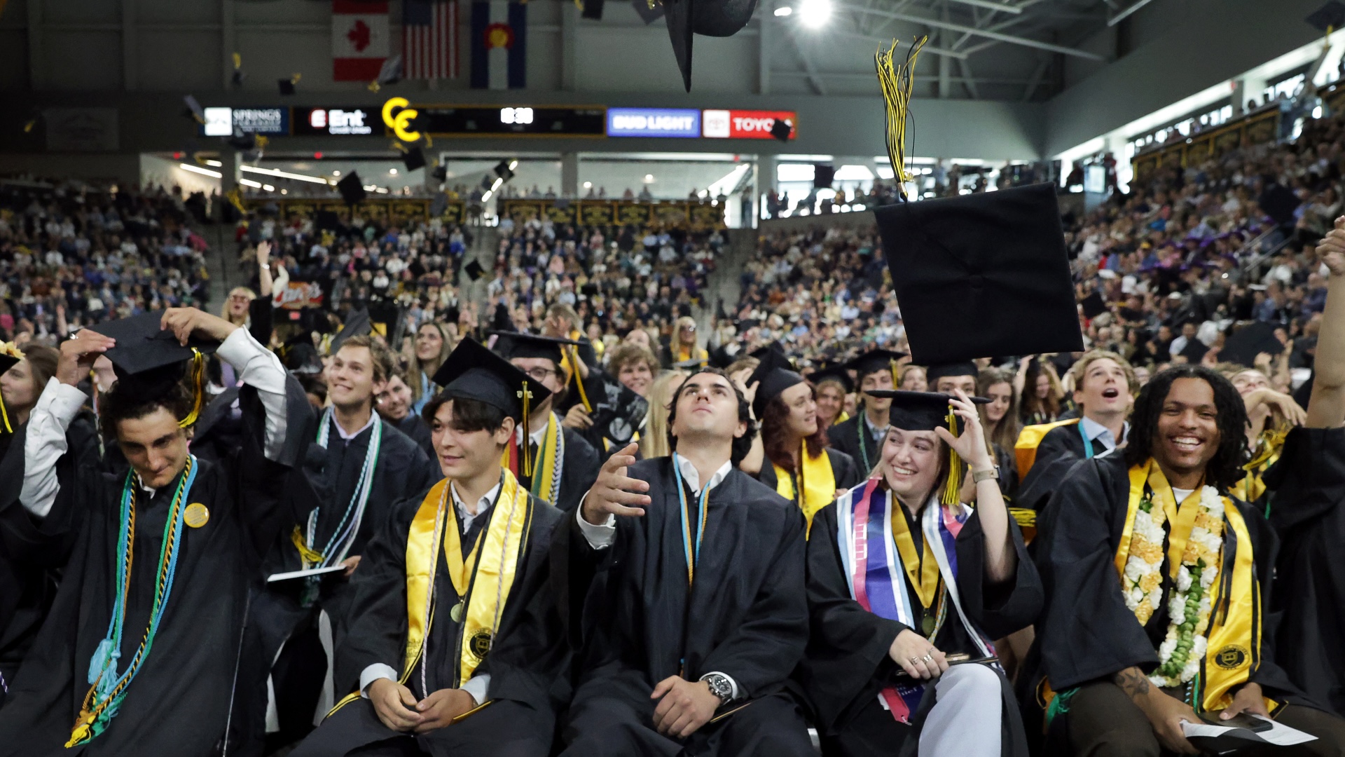 graduates in regalia seated in Robson arena toss their graduation caps in celebration