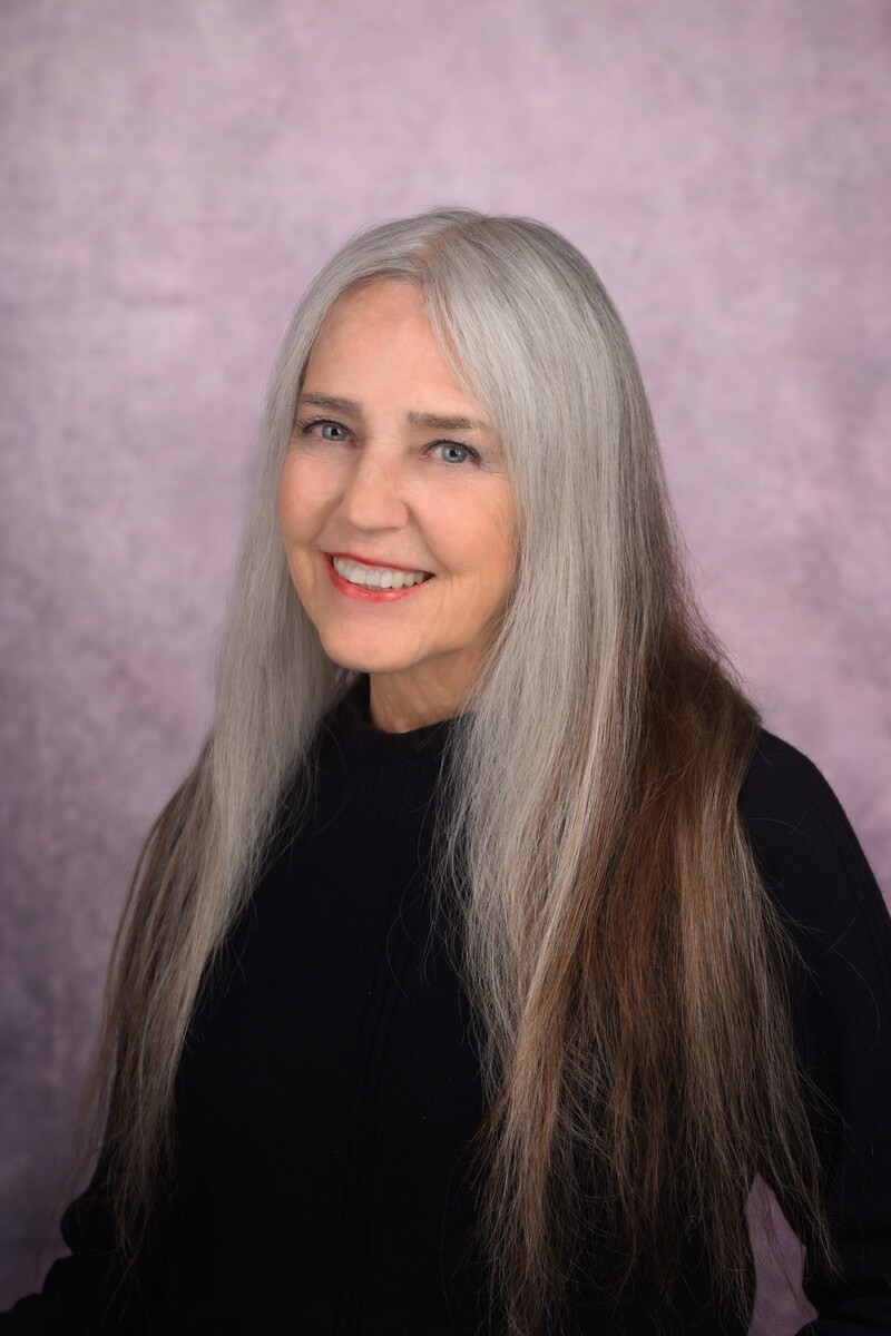 Image of Gypsy Ames, smiling and in a black outfit against a soft pink background. 