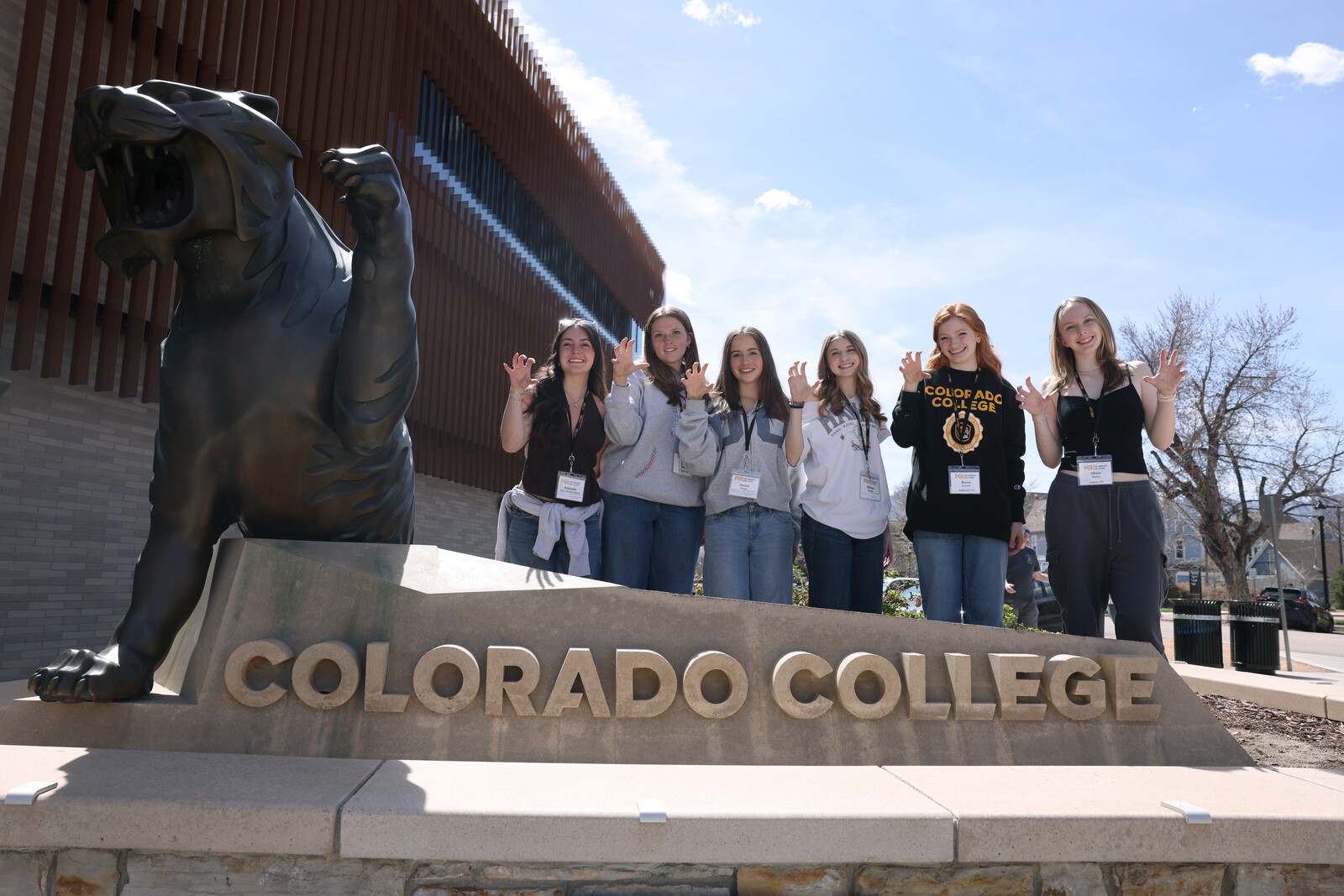 Prospective students pose next to a tiger statue and Colorado College sign making tiger claws with their hands.