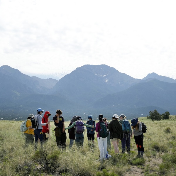 A class gathers standing in a field with mountains dramatically silhouetted behind them