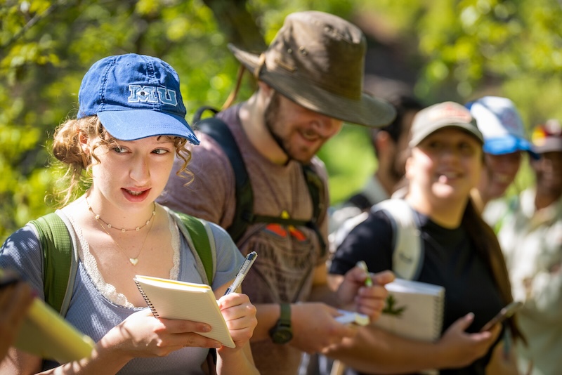 a female student takes notes outside with her class