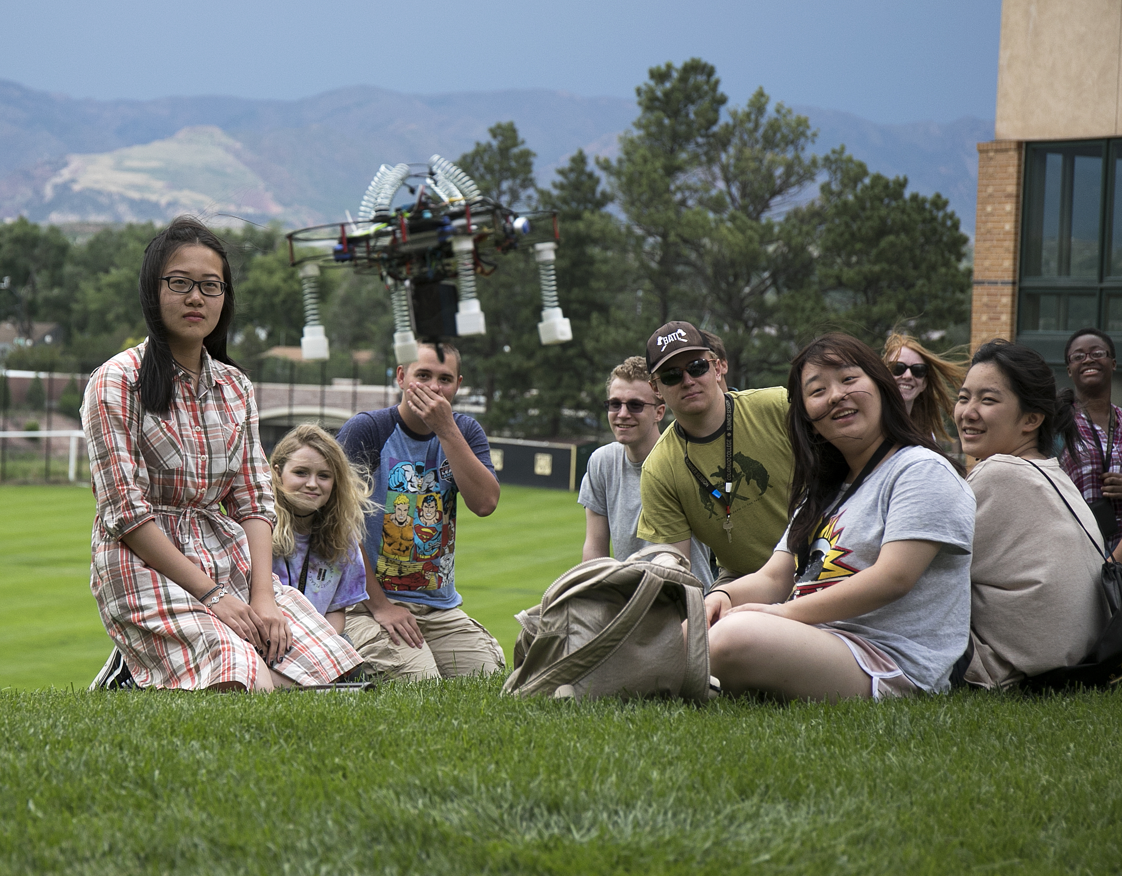 Group of students sitting on the grass outside with a drone.