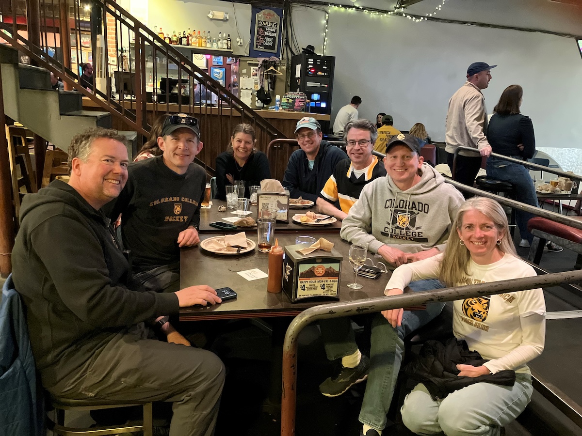 7 CC alumni sitting around a table enjoying food, drinks, and each others' company